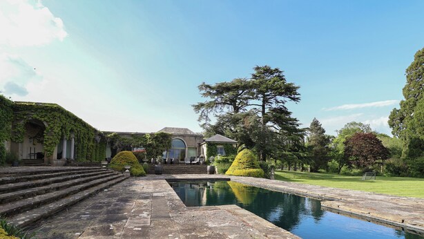 A pool with stone steps leading to a building with arched doorways and a gazebo.
