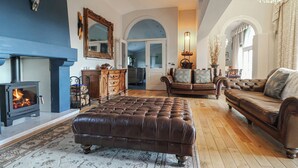 A spacious living room with a fireplace, leather sofas, a large ottoman, and a chandelier.