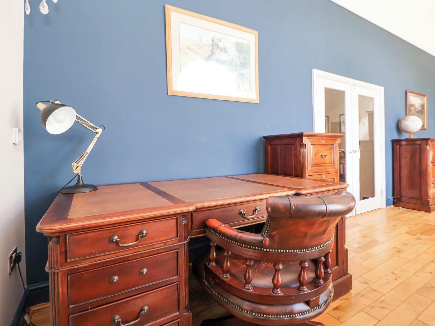 Une pièce comprenant un bureau en bois, un fauteuil en cuir, une lampe et une commode.