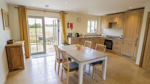 Une cuisine moderne avec des meubles en bois, une table à manger avec des chaises et une porte-fenêtre coulissante donnant sur un espace extérieur.