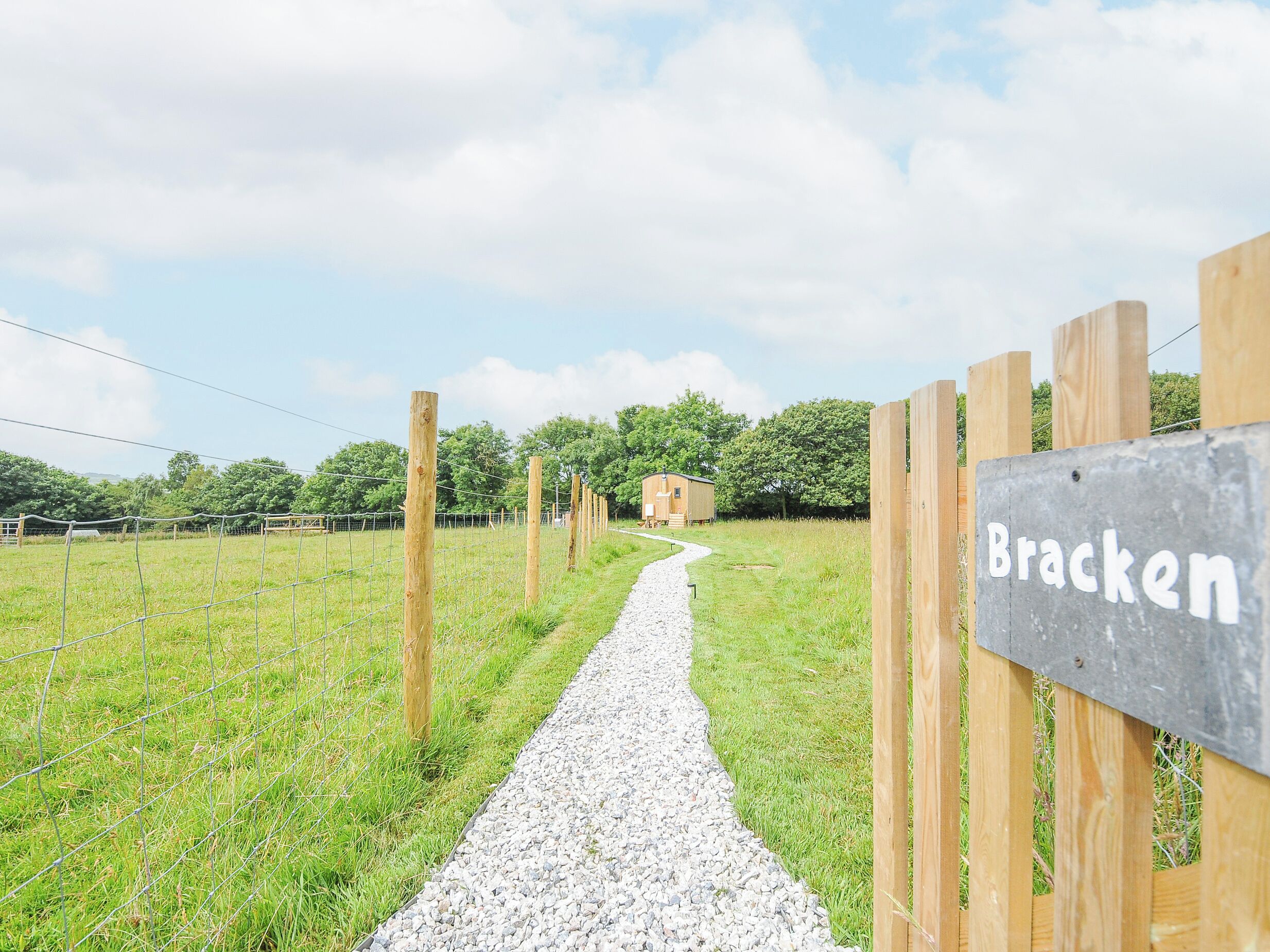 A gravel path leading to a wooden fence with a sign reading "Bracken."