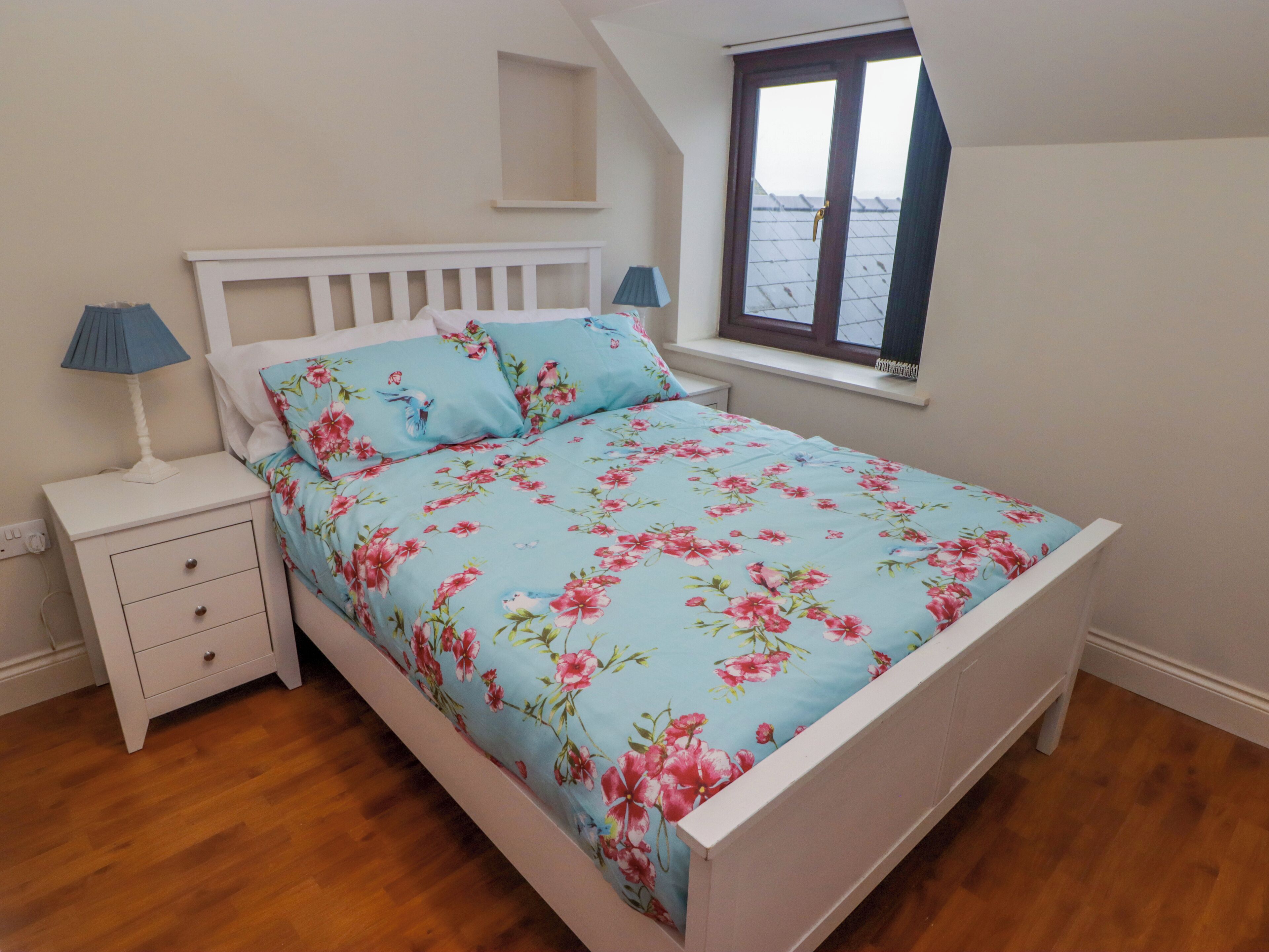 Ein Schlafzimmer mit einem Bett, Nachttischen, einem Fenster und Holzboden.