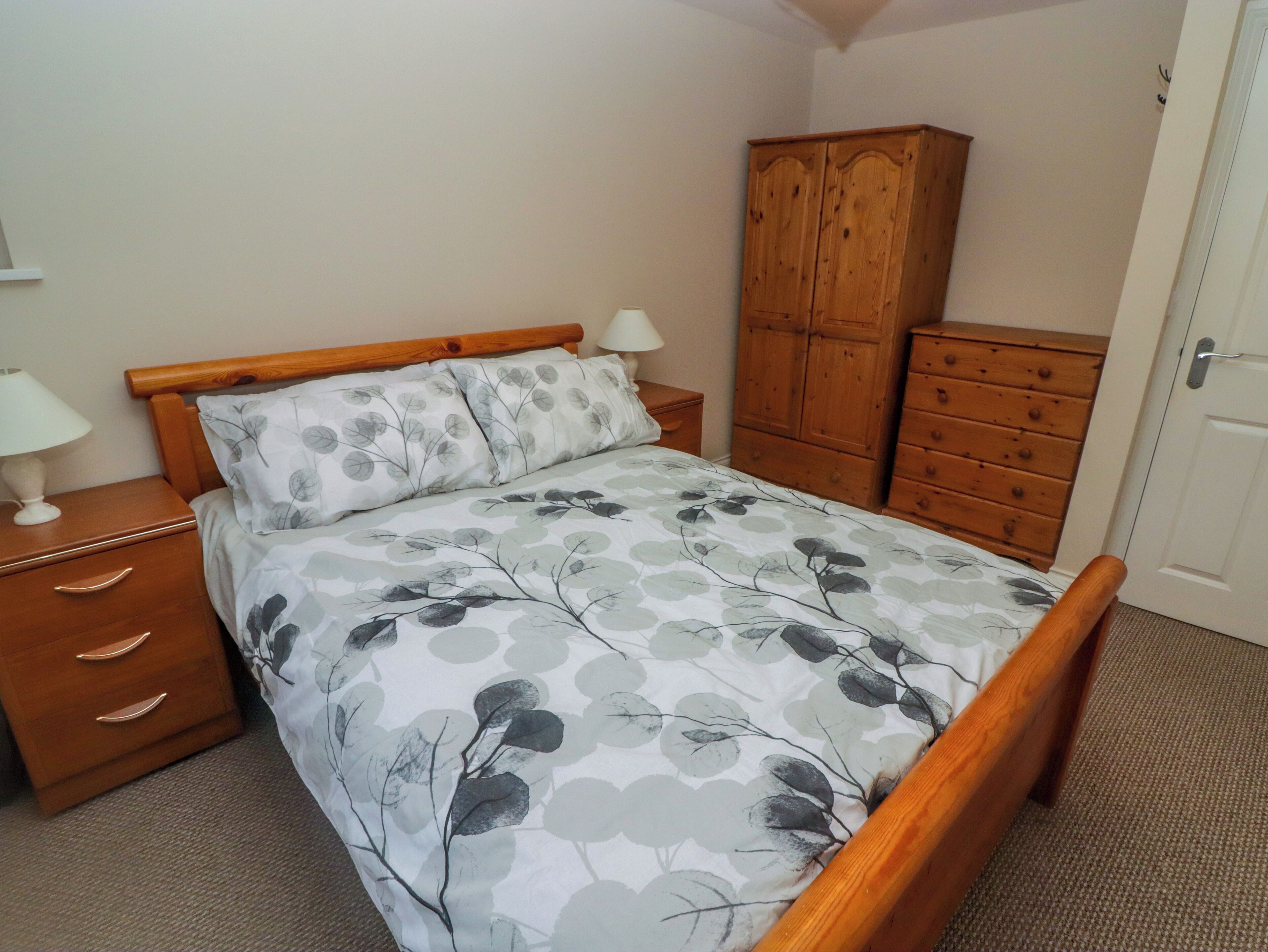 A bedroom with a bed, wooden nightstand, dresser, and wardrobe.
