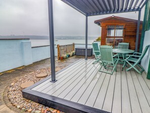 Eine überdachte Terrasse mit einer Holzhütte, grünen Stühlen und einem Tisch.