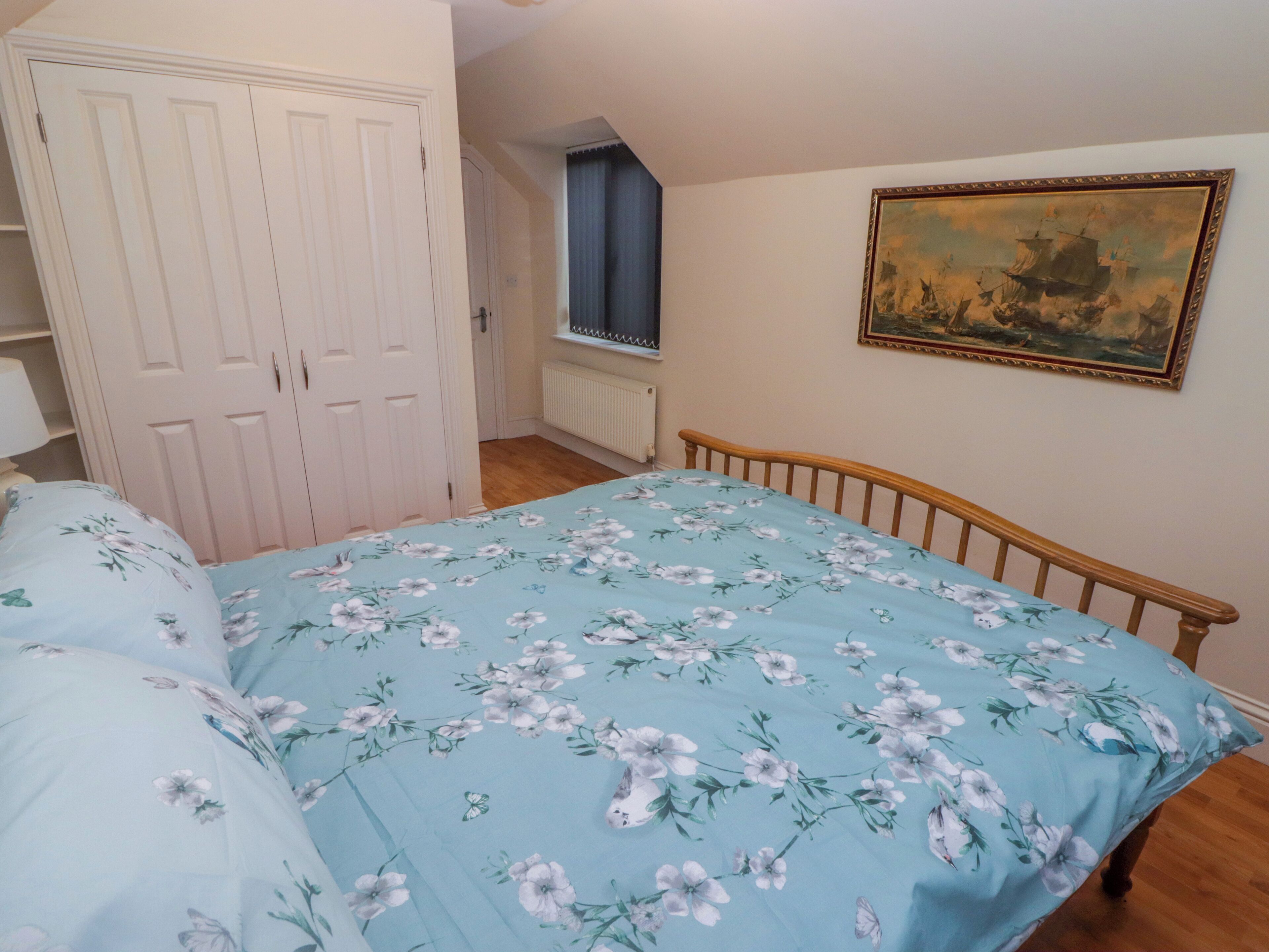 A bedroom with a bed, a wardrobe, a window with curtains, and a painting on the wall.