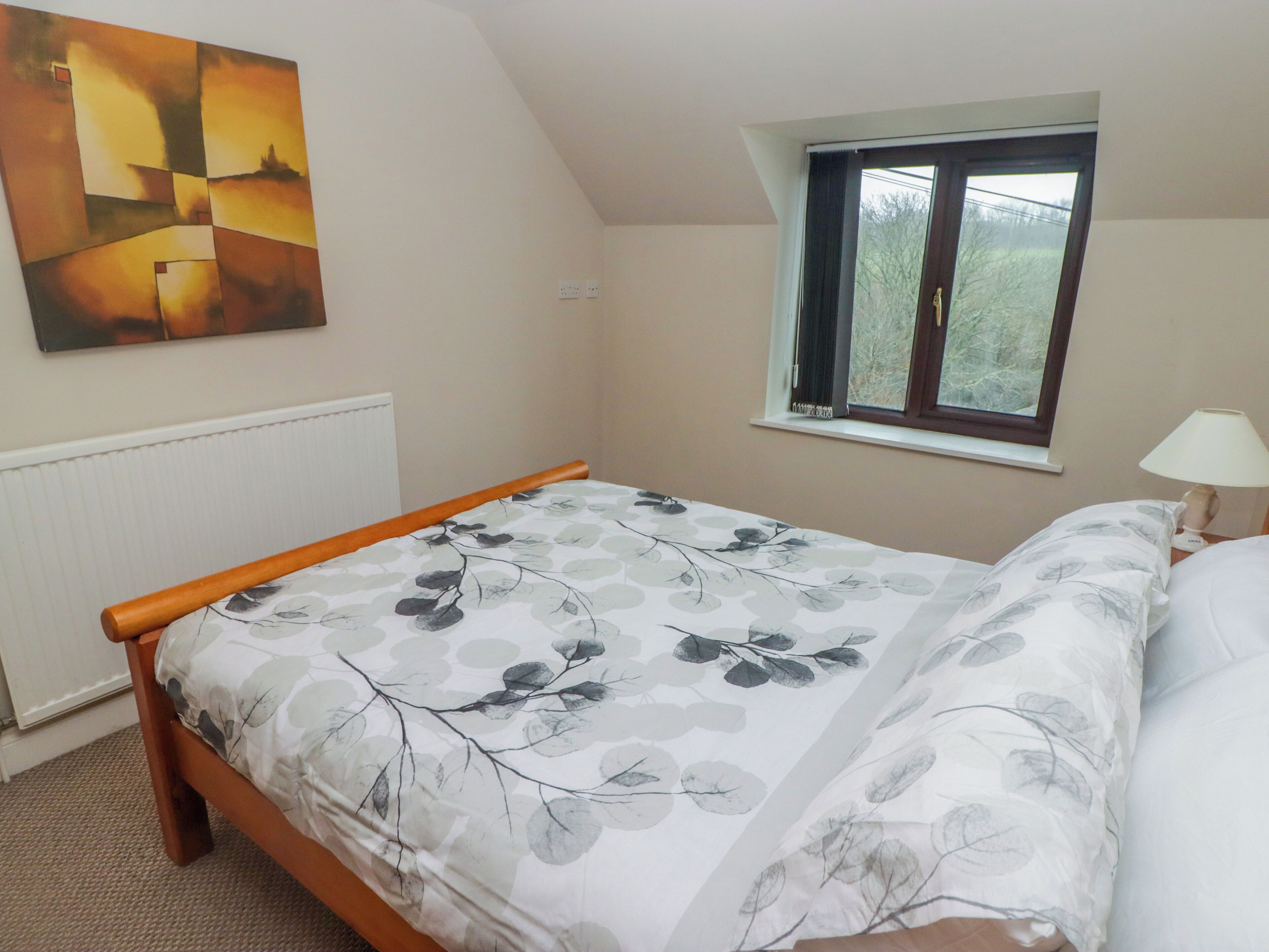A bedroom with a bed, a window, a radiator, and a painting on the wall.