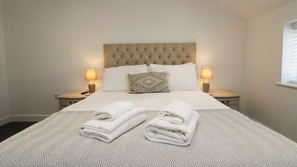 A neatly made bed with a patterned bedspread, two bedside lamps, and a decorative pillow. - Edgemere Hideaway (Grange-over-Sands)