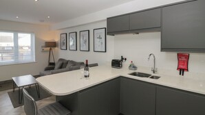 A modern kitchen with a central island, grey cabinets, a built-in sink, and a fire blanket sign. - Edgemere Hideaway (Grange-over-Sands)