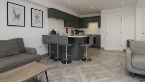 A modern kitchen with a bar area, a grey sofa, and a dining table. - Edgemere Hideaway (Grange-over-Sands)