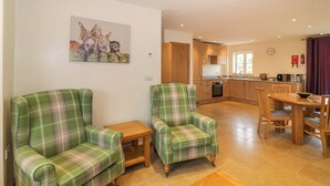 Een woonkamer met twee groene gestreepte fauteuils, een houten salontafel en een schilderij van paarden aan de muur.