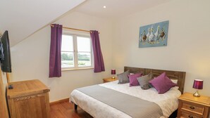 Une chambre à coucher avec un lit, des tables de chevet en bois, une télévision et une fenêtre ornée de rideaux violets.
