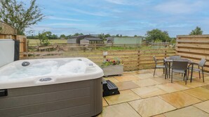 Een jacuzzi op een terras met uitzicht op een boerderij en een houten hek.