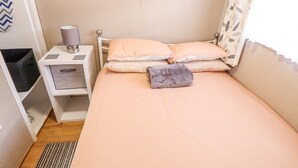 Un dormitorio pequeño y ordenado, con una cama, almohadas, una mesita de noche con una lámpara y un mueble para guardar objetos.