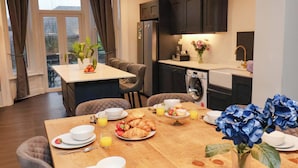 A dining area with a wooden table set for breakfast, including croissants, strawberries, and orange juice. There is a small kitchen area with a washing machine and cabinets. - Wellington Lodge (Bridlington)
