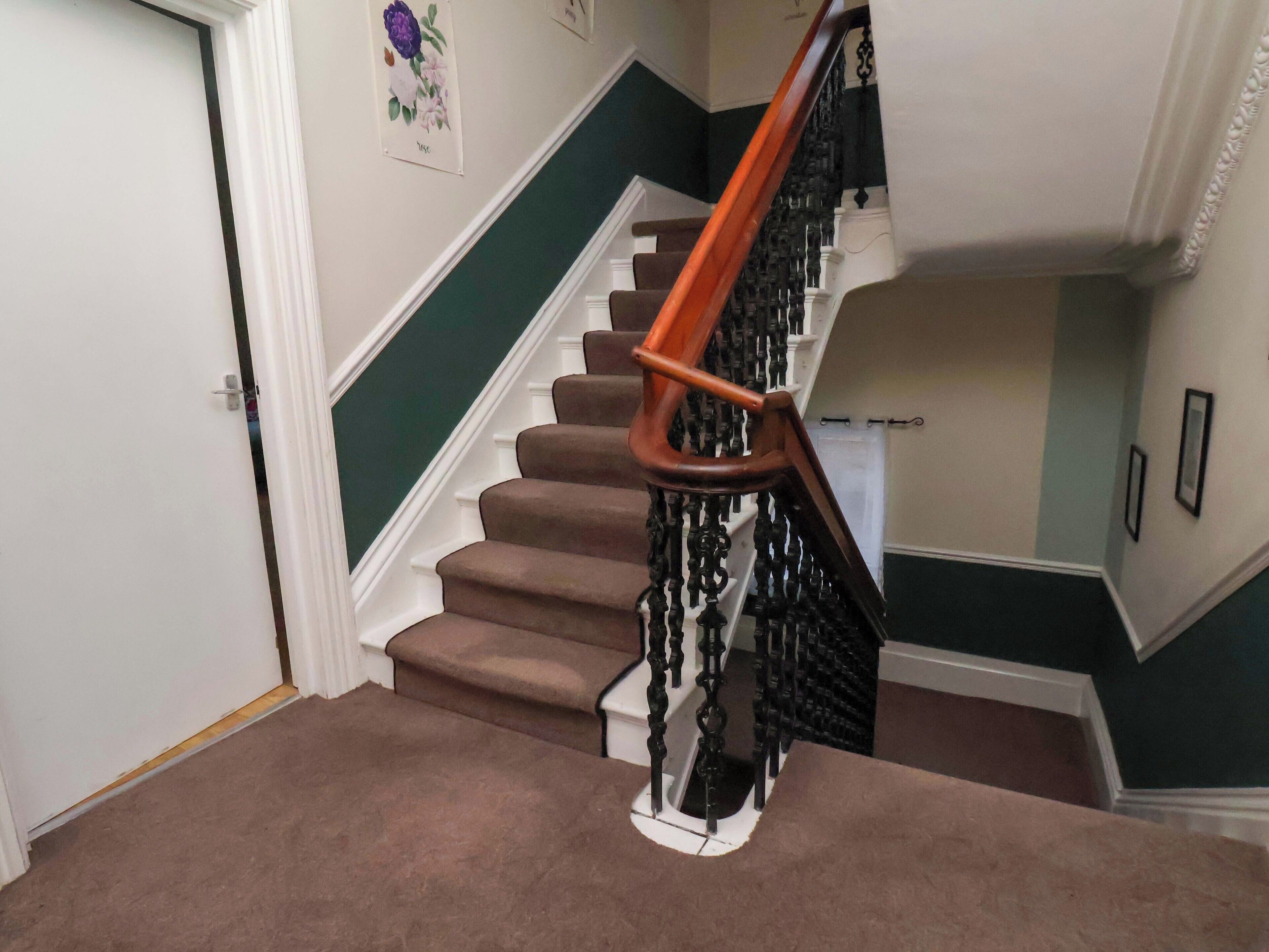 Un escalier avec une rampe en bois et des balustres noires, des marches recouvertes de moquette et un mur vert.