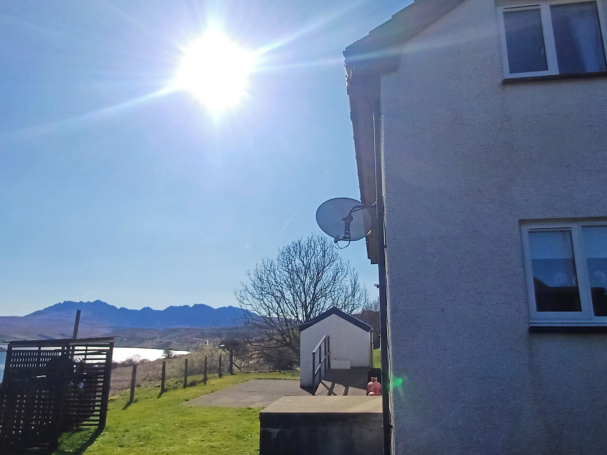 A house with a satellite dish, a clear sky, and mountains in the background.
