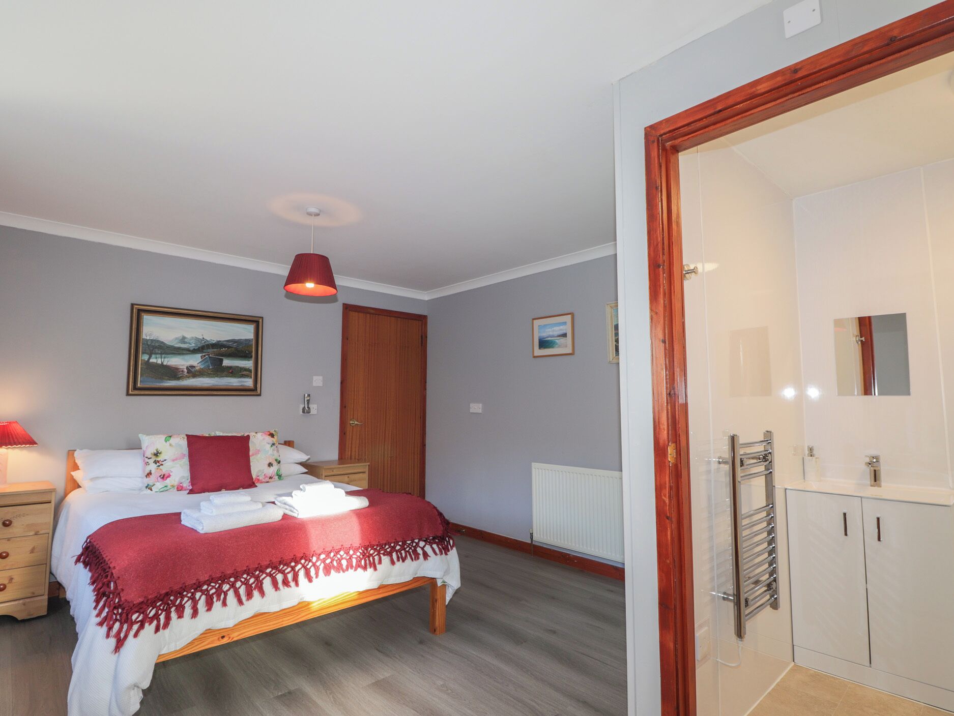 A bedroom with a bed, bedside table, lamp, and a door leading to a bathroom.