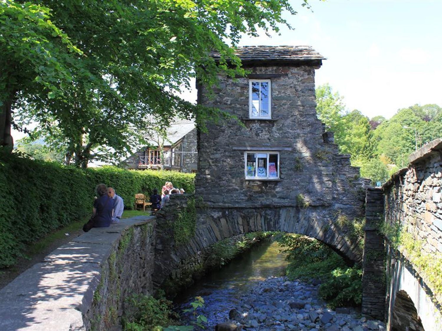 A stone bridge over a stream with a small building on the right.