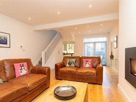 A spacious living room with two leather sofas, a wooden coffee table, and a fireplace. A staircase leads to an upper level.