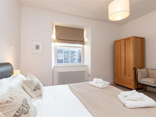 A bedroom with a bed, a window with a view, a radiator, a wooden wardrobe, and a chair.
