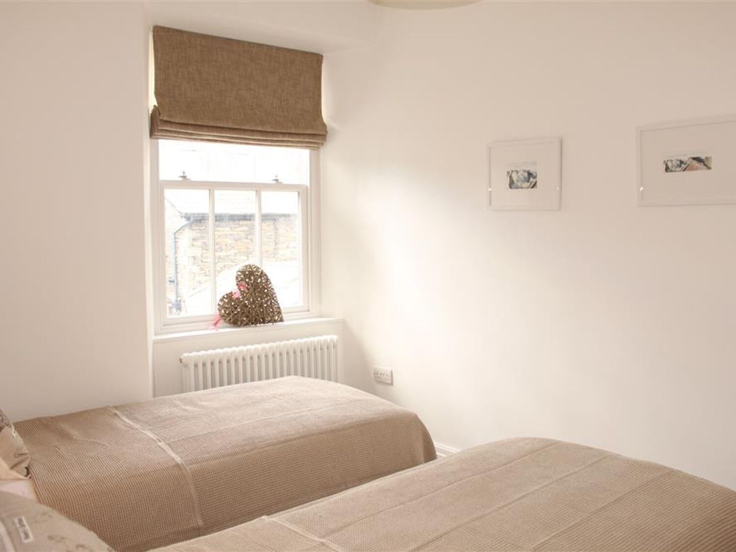 Un dormitorio con dos camas, una ventana con vistas a edificios y dos cuadros en la pared.