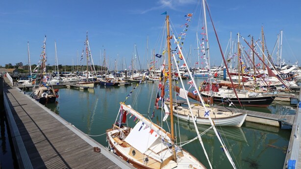 Un port de plaisance où sont amarrés de nombreux bateaux, avec des passerelles en bois et des drapeaux.