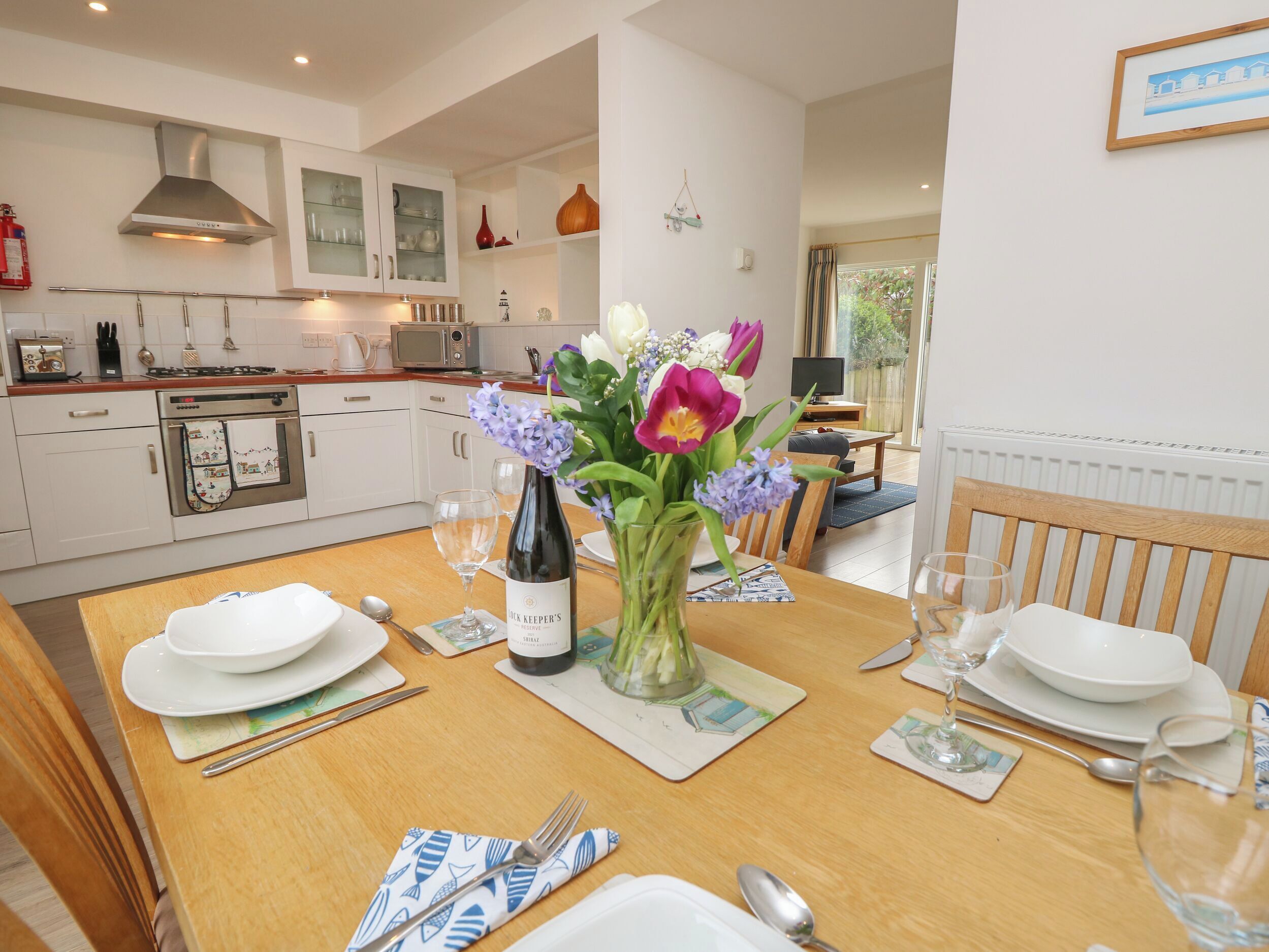 A dining table set with plates, glasses, and a bottle of wine, with a vase of flowers in the center.