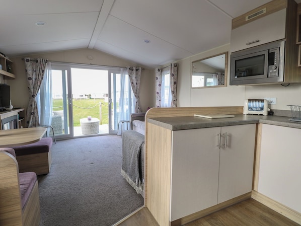 A compact kitchenette with a microwave, toaster, and a small dining area with a table and chairs. - Coastal Retreat (Norwich)