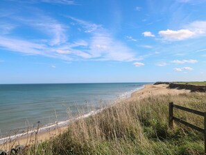 A beach with a wooden fence, grassy dunes, and a clear sky. - Coastal Retreat (Norwich)
