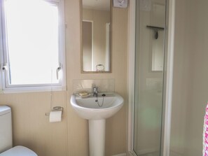 Une salle de bain avec un lavabo blanc, un miroir, des toilettes et une cabine de douche en verre.