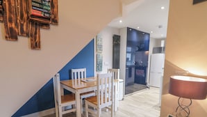 A modern kitchen with white appliances, a dining area with wooden chairs, and a blue accent wall. - The Corner House (Londonderry)