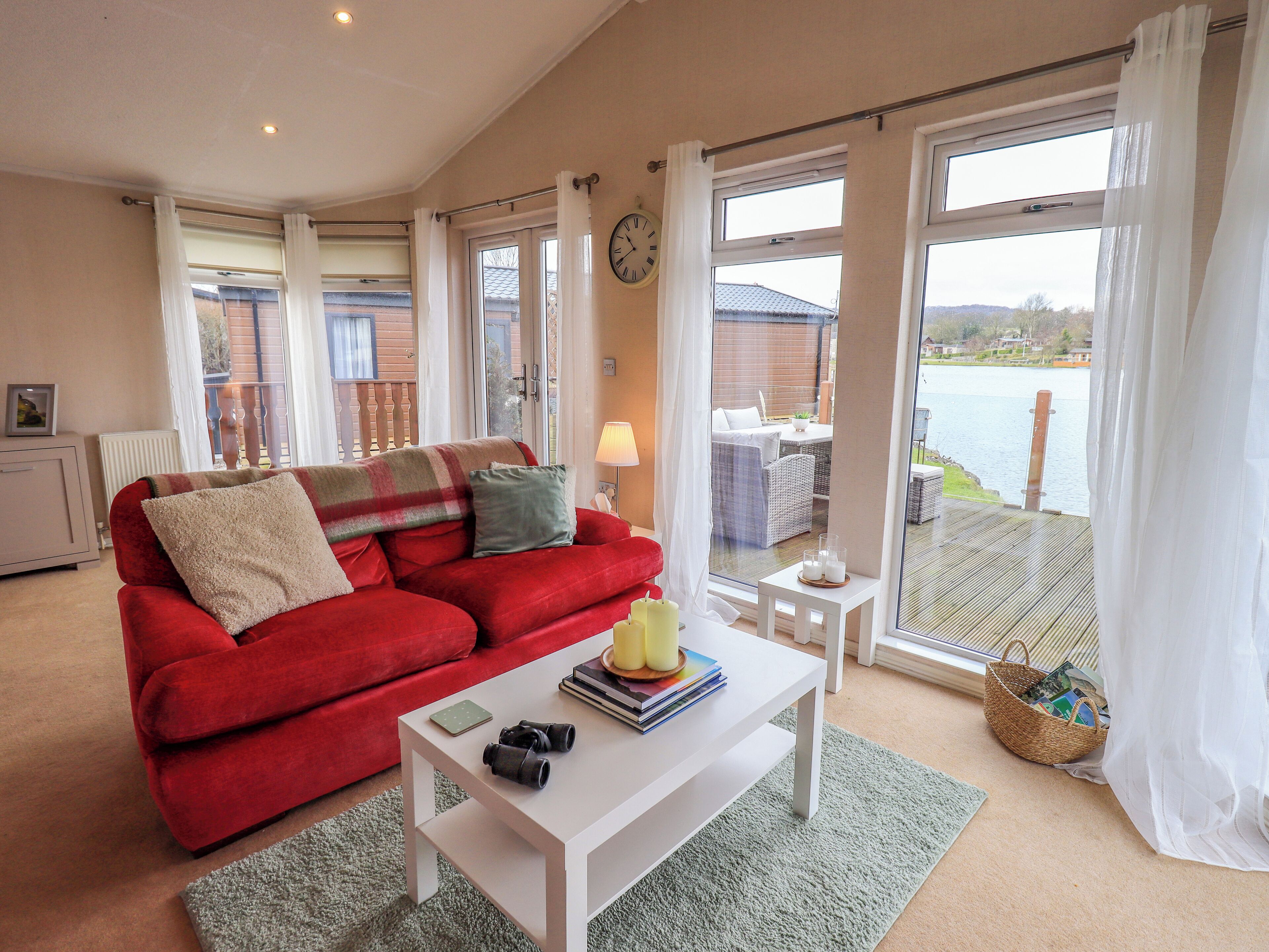 A living room with a red sofa, a white coffee table, and a view of a balcony with outdoor furniture.