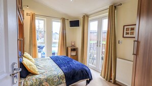 Un dormitorio con cama, cortinas, un radiador y un televisor en la pared.