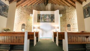 A church interior with wooden pews, a stone wall, and a central altar. - Myddelton Grange (Ilkley)