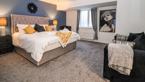A modern bedroom with a large bed, bedside lamps, a dark-colored sofa, and a large window with curtains. - Myddelton Grange (Ilkley)