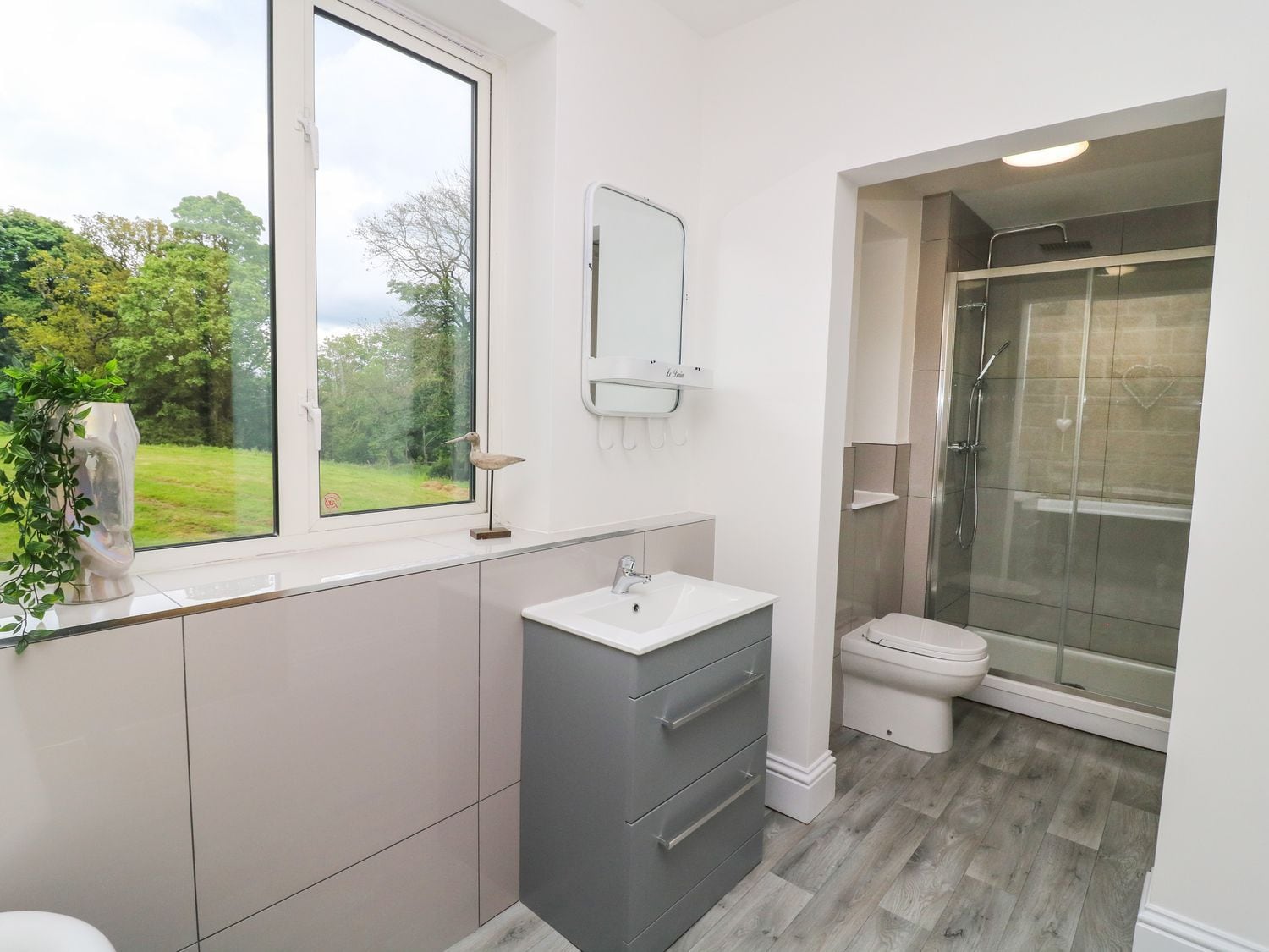 A modern bathroom with a window, a sink, a toilet, and a shower.