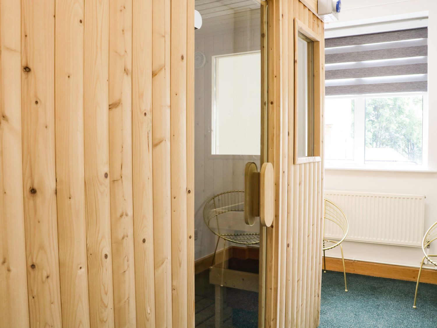 A wooden room with a large window, a radiator, and two metal chairs.