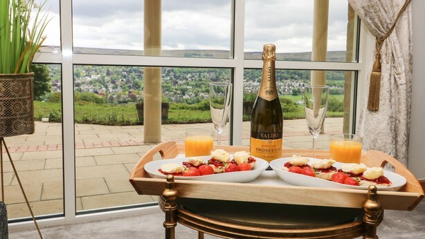 A table with two plates of strawberries and cream, a bottle of Valdo Prosecco, and two glasses of orange juice, set against a scenic view. - Myddelton Grange (Ilkley)