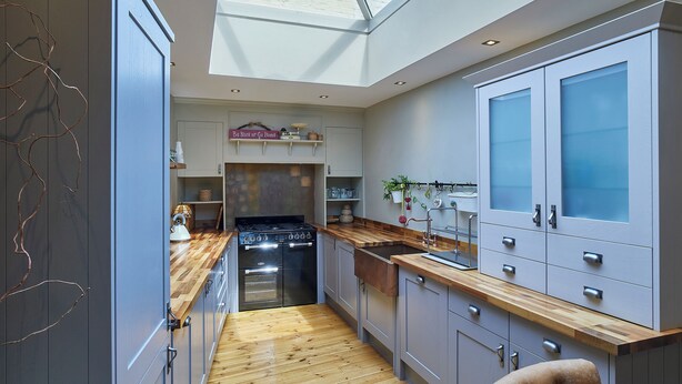 A modern kitchen with a skylight, wooden flooring, and grey cabinetry.
