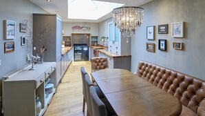 A modern kitchen with a central island, a dining area with a large wooden table and leather booth seating, and a skylight above.