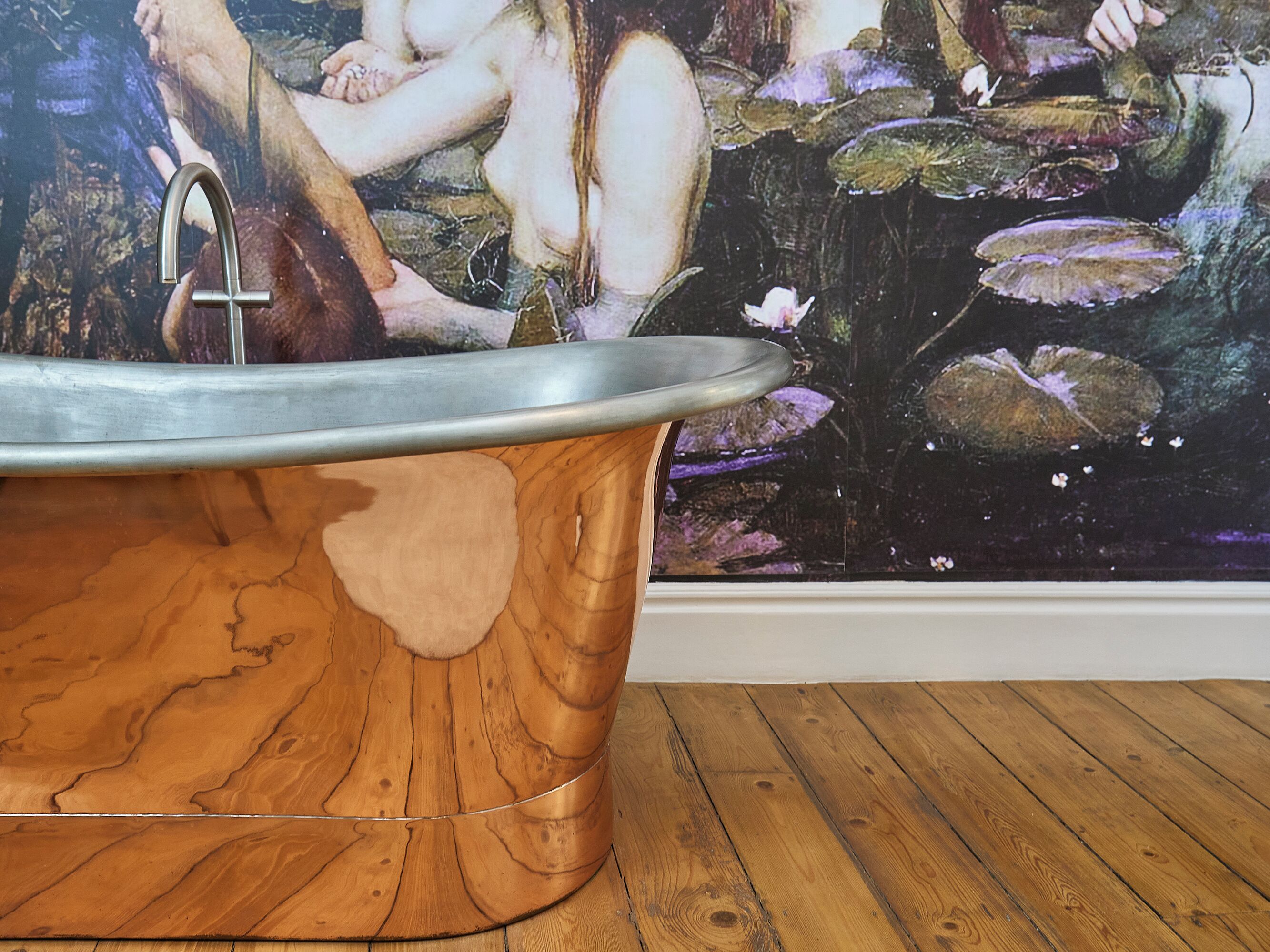 A bathtub with a wooden finish and a faucet, positioned in front of a mural depicting a pond with lily pads and a figure.
