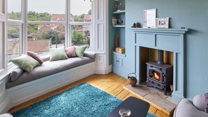 A cozy room with a large window seat, a fireplace, and a chandelier.