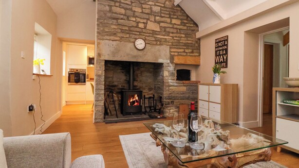 A living room with a stone fireplace, a glass coffee table, and a sofa. - Honeysuckle Cottage (Somerton)