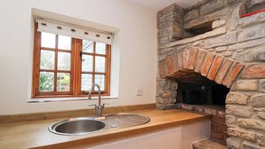 A kitchen with a stone oven, a sink, and a window with blinds. - Honeysuckle Cottage (Somerton)