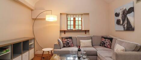 A cozy living room with a glass coffee table, a sofa, a floor lamp, and a painting on the wall.