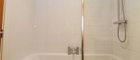 A modern bathroom with a glass-enclosed shower, a standalone bathtub, and white tiled walls.
