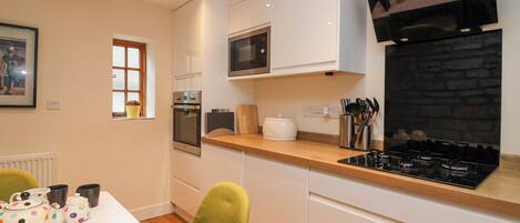 A modern kitchen with white cabinetry, a built-in oven, a microwave, a gas stove, and a stone fireplace.