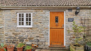 A stone cottage with a tiled roof, a wooden front door, a window, and a sign reading "Honeysuckle Cottage". - Honeysuckle Cottage (Somerton)