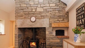 A stone fireplace with a clock above it, a wooden cabinet to the right, and a wall with a motivational quote. - Honeysuckle Cottage (Somerton)