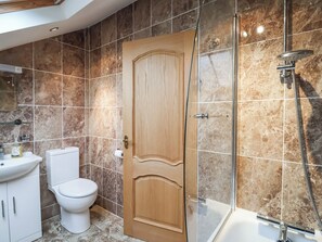 Une salle de bain avec une porte en bois, des toilettes, un lavabo et un espace douche doté d’une porte en verre.